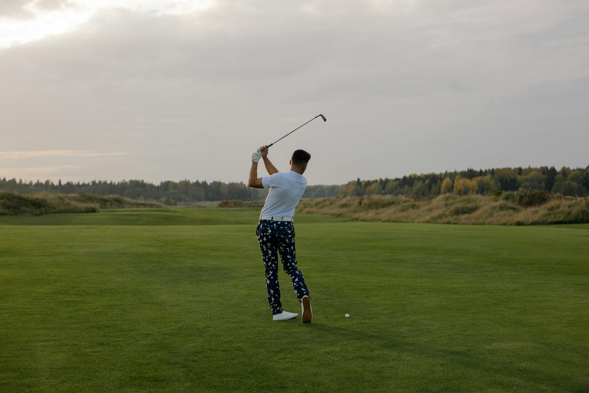 Golfer viewed from behind completing iron swing on open fairway