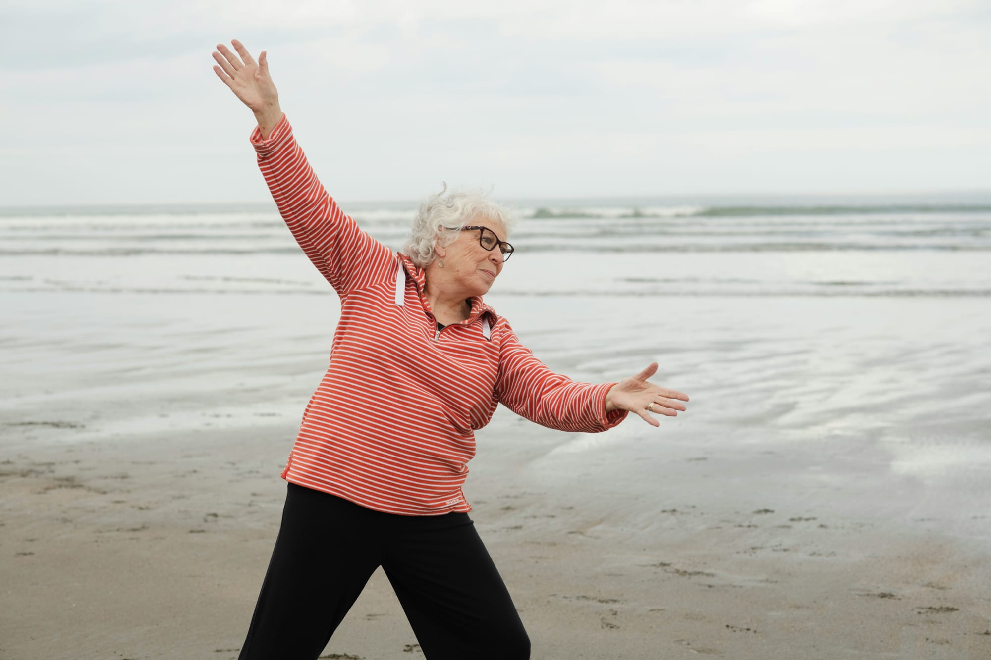 Senior woman in balance pose with arms extended on beach