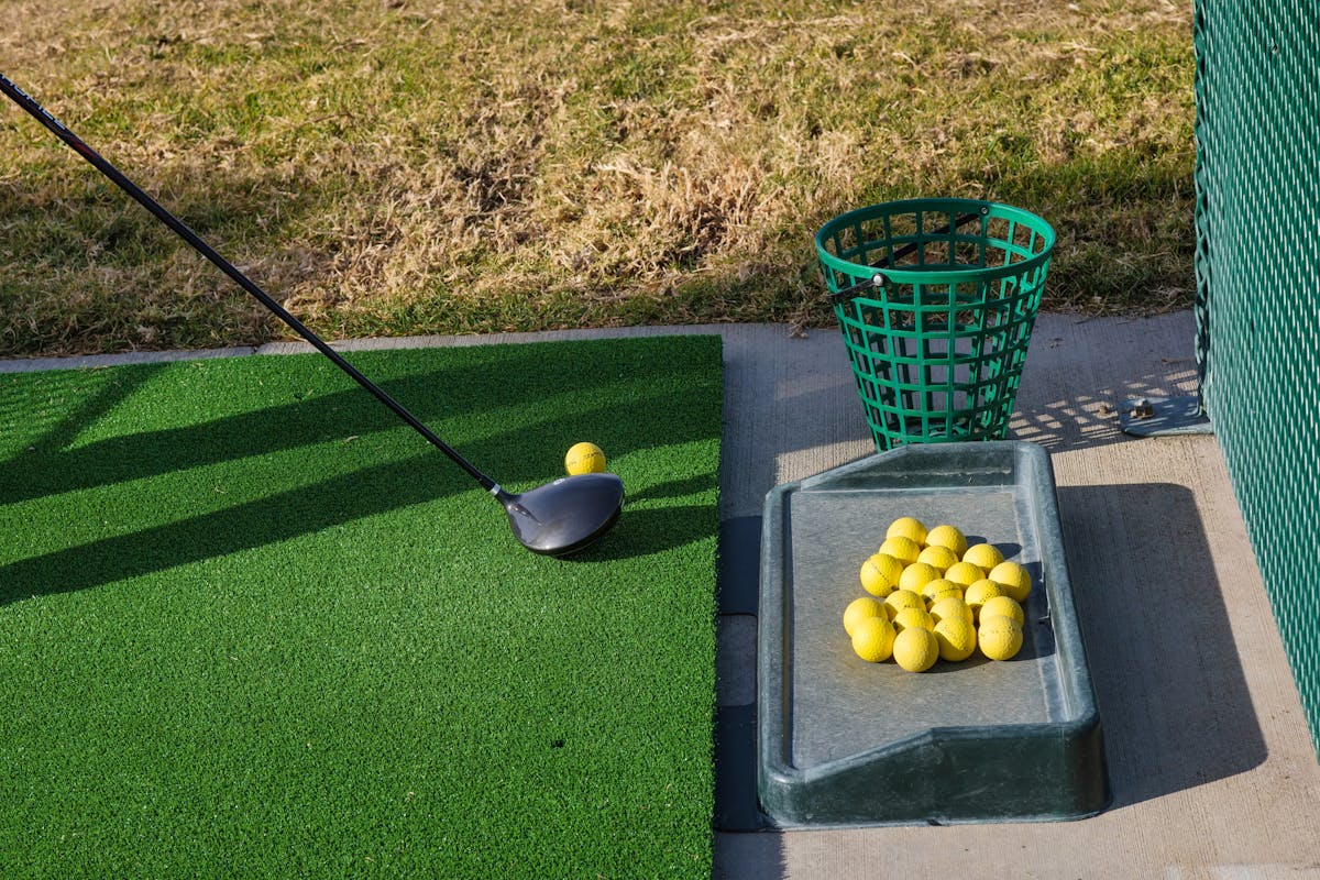 Golf driving range mat with club and yellow practice balls set up