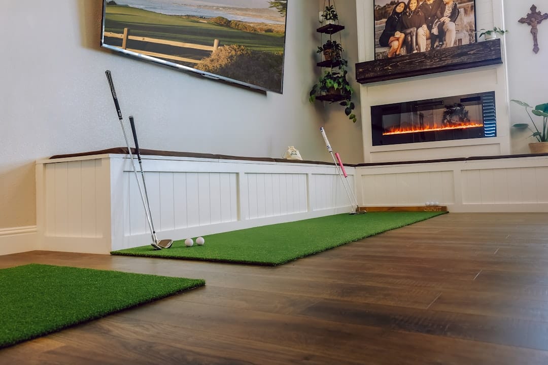 Indoor golf practice room with putting mats on wooden floor and large wall display