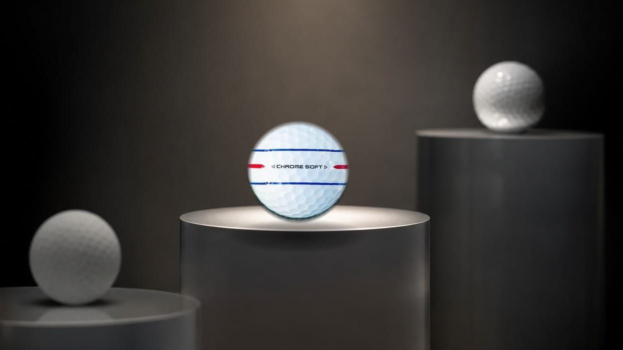 Three ascending retail-shelf risers with a Callaway Chrome Soft golf ball spotlit on the middle riser, a soft-focus value ball lower left and a tour ball higher right