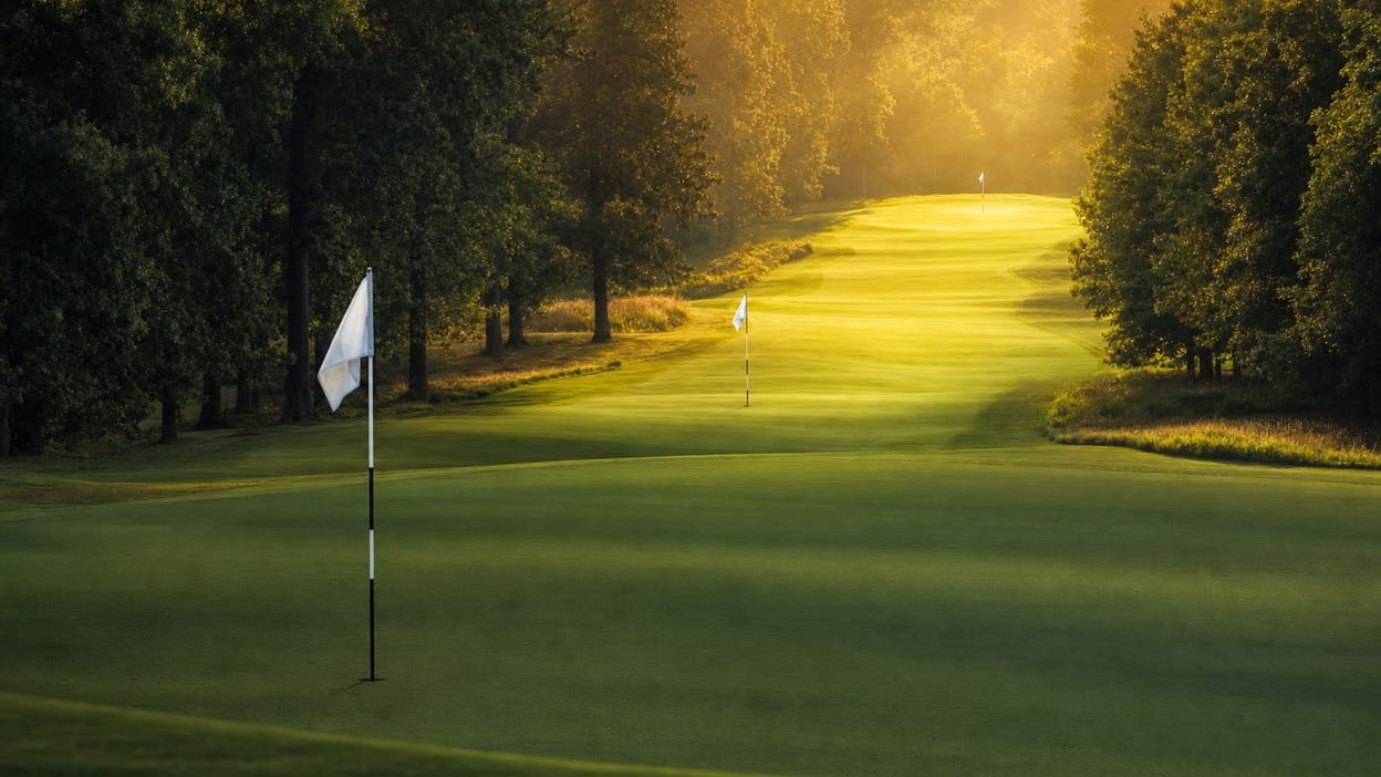 Golf course fairway with three flagsticks receding into warm evening light