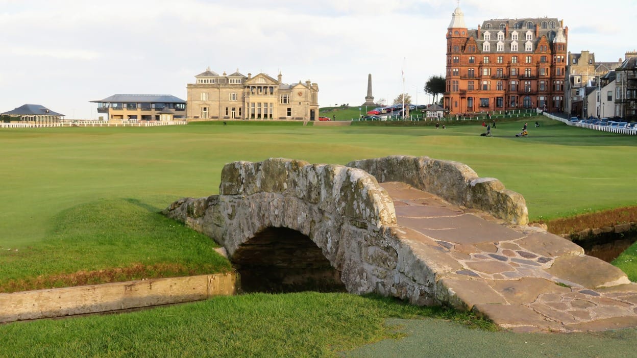 The stone Swilcan Bridge on the 18th hole at St Andrews Old Course, with the R and A clubhouse and Old Course Hotel in the background.