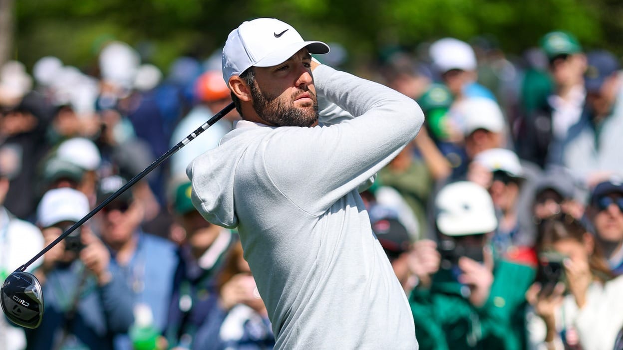 Scottie Scheffler mid-swing with driver, follow-through pose, gallery blurred in background; file photo from the 2024 Masters.