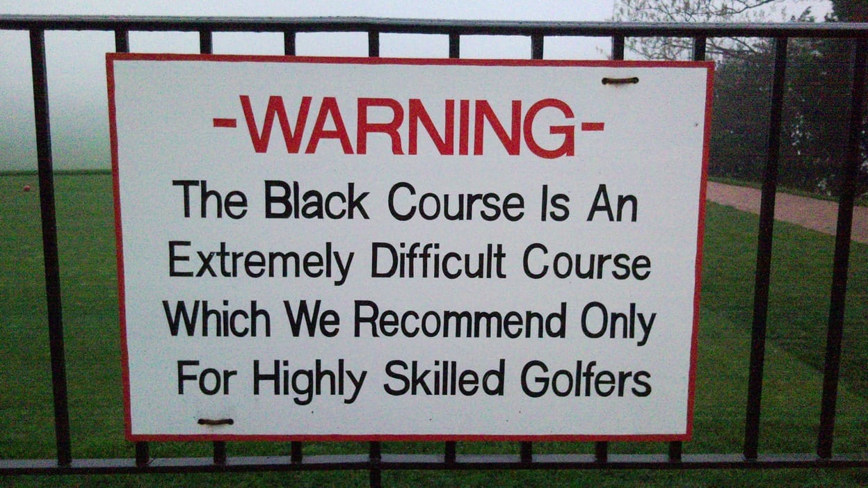 Warning sign on a fence at Bethpage Black Course reading that the Black Course is an extremely difficult course recommended only for highly skilled golfers