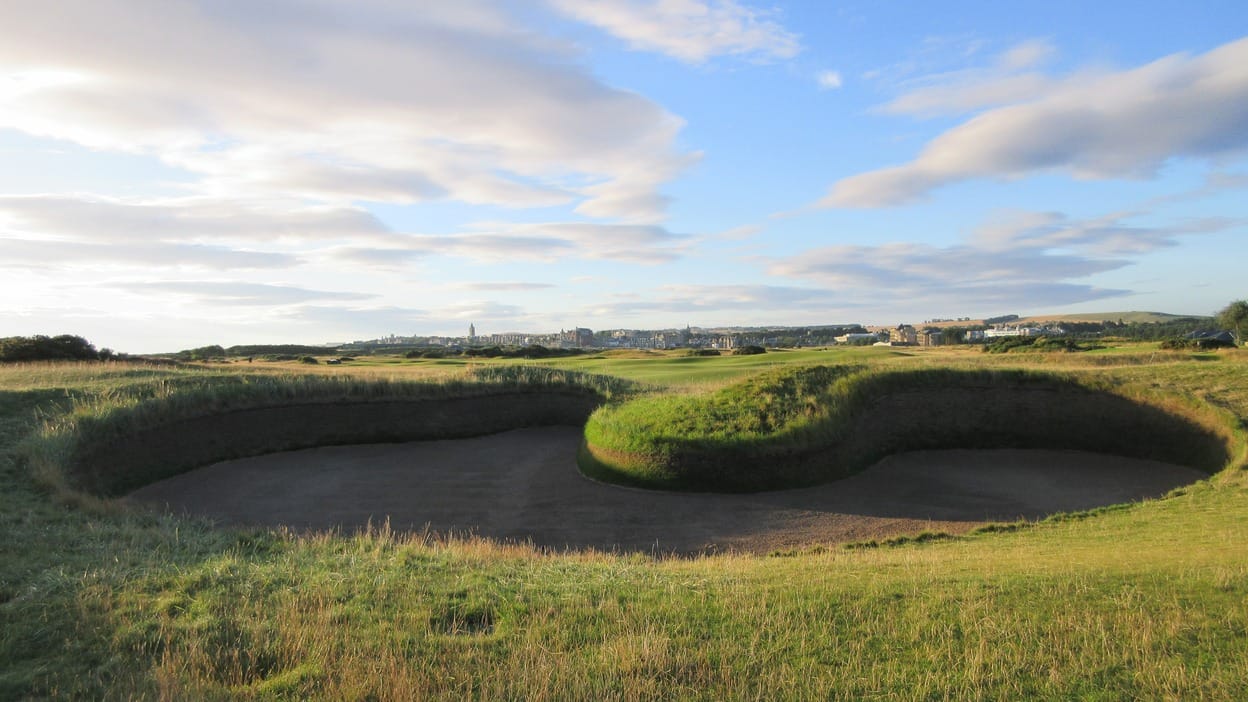Hell Bunker, a deep sand hazard on the fourteenth hole of the Old Course at St Andrews, with the town skyline beyond in morning light.