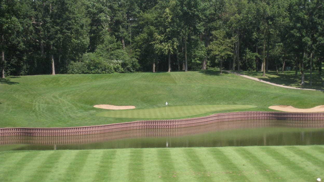 A par-3 over Lake Kadijah on Medinah Country Club's Course No. 3, the green framed by bunkers and trees across the water.