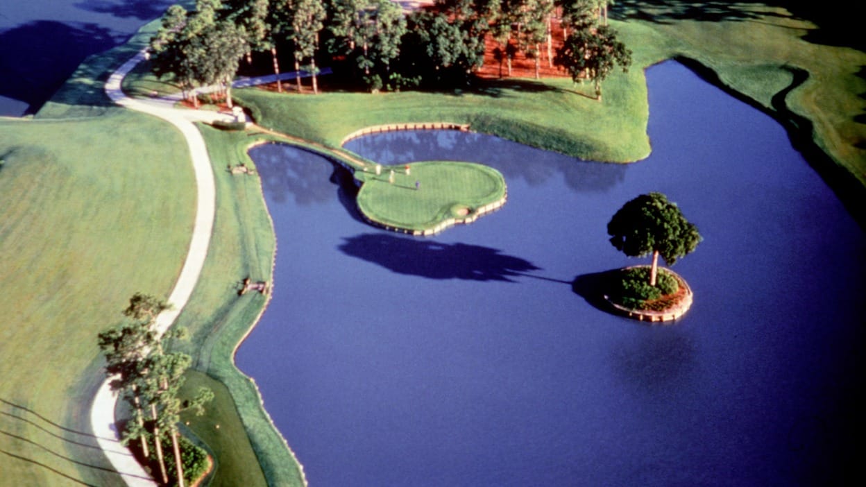 Aerial view of the par-3 17th hole at TPC Sawgrass, the iconic island green surrounded by water with a single tree on a small island beside it.