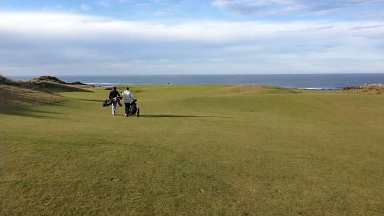 Golfers walking the fairway toward the 4th green at Bandon Dunes Golf Resort, with the Pacific Ocean along the coastline in the background.