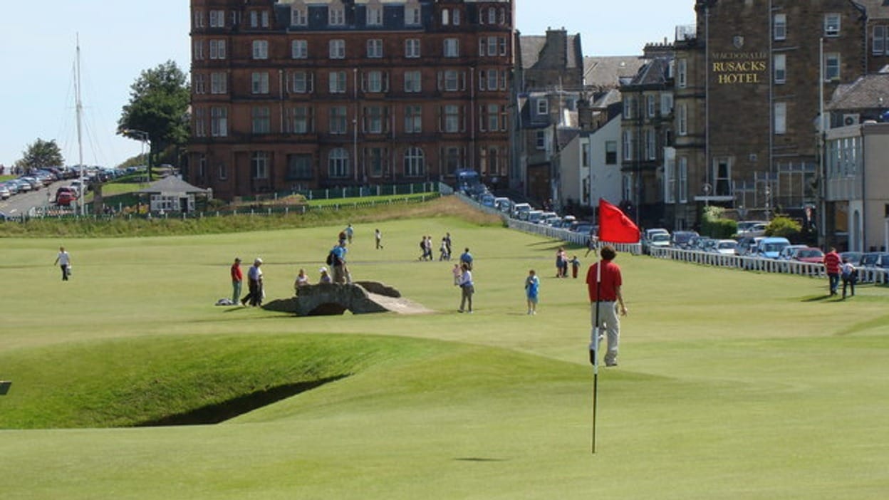 The 17th green on the Old Course at St Andrews, with a red flagstick, the Rusacks Hotel beyond, and golfers walking the fairway, photographed in 2007.